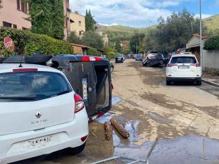 In primo piano macchina ribaltata e con i vetri distrutti, a causa della forza dell\'acqua, mentre sullo sfondo macchine ammassate l\'una sull\'altra.