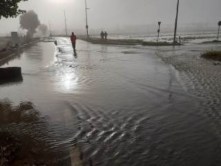 Strada e campi allagati con persone sul posto