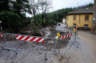 Strada con transenne per delimitare la strada sconnessa e con detriti portati dall\'acqua. Palo divelto.