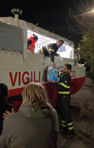 Operatori di Croce Rossa e Vigili del fuoco che dal mezzo anfibio consegnano acqua e cibo alle persone sfollate