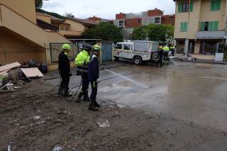 Operatori mentre puliscono la strada di fronte al condominio dal fango accumulato post alluvione e spostamento di rifiuti alluvionati