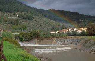 Bisenzio con poca acqua in zona Cavalciotto, sullo sfondo la montagna il cielo scuro e un accenno di arcobaleno